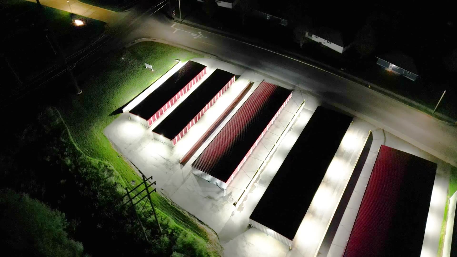 Aerial drone view at night of a brightly lit self-storage facility with LED lighting on every building